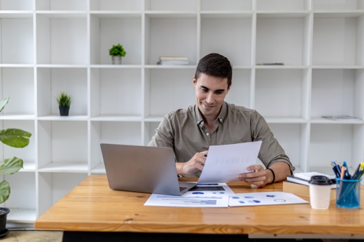 A young businessman sitting in the office working with a laptop, he is checking financial documents, he founded a startup, he is a young entrepreneur who has the skills to run a growing company.