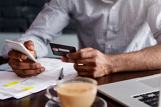 Man using cellphone and card in front a laptop and a coffee