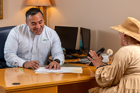 A man and a woman are seated at a desk, discussing details of a checking account.