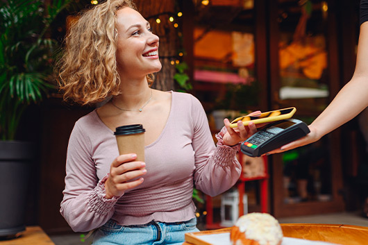 A woman with a coffee in one hand and a credit card in the other, representing mobile payment methods in Hebbronville.